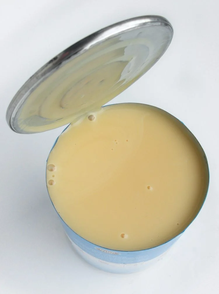 An opened tin of condensed milk with a spoon